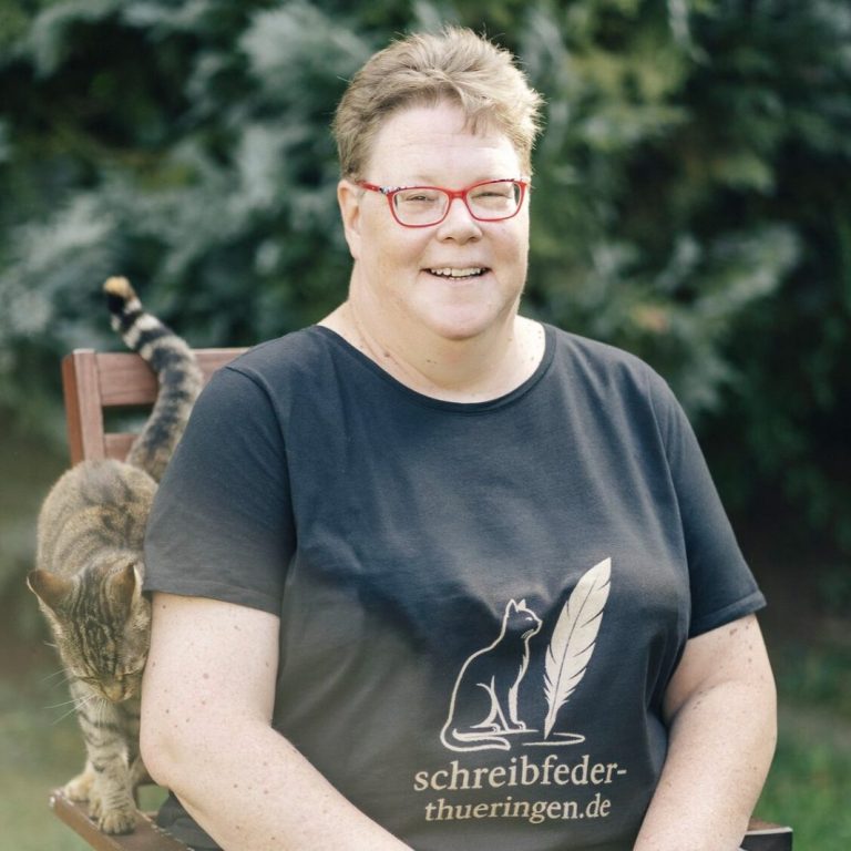 zwei Katzen auf dem Schreibtisch zwischen Büchern