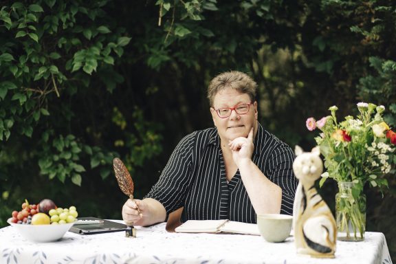 Ideen im Kopf Geli sitzt mit Schreibfeder und Notizbuch an einem Tisch im Garten.